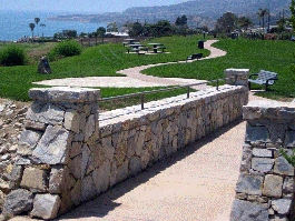 Stone bridge leading to grass area and trail with benches, tables and view of ocean